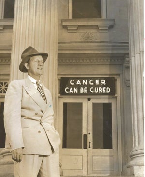 Attorney Ed Reid is shown in front of a neon sign, reading “Cancer can be cured.” 