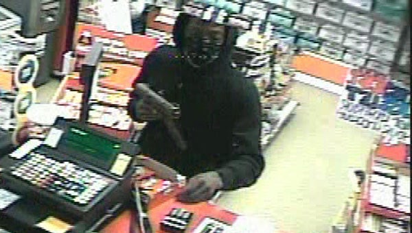 The suspect is seen reaching for the cash register with one hand, while holding a gun in the other.