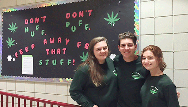 Peer Helpers Haley Booker, Charlie Brock and Clorissa Morgan with a bulletin board promoting ‘Stay Off the Grass.’